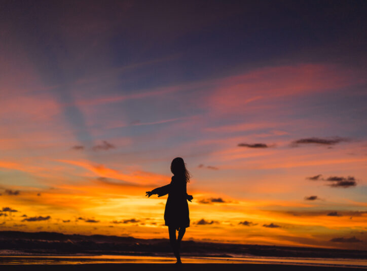 people on the beach at sunset. the girl is jumping against the backdrop of the setting sun.